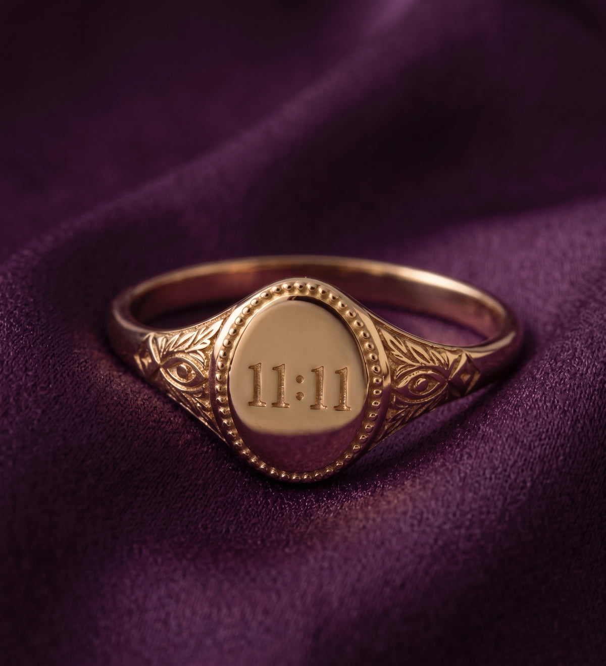 Oval signet ring engraved with 11:11 on purple velvet, front view
