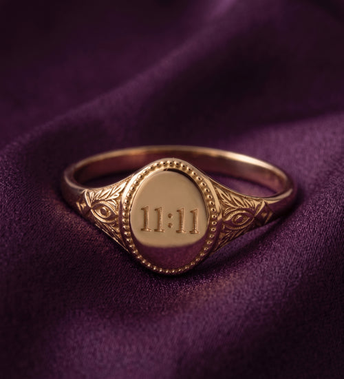 Oval signet ring engraved with 11:11 on purple velvet, front view