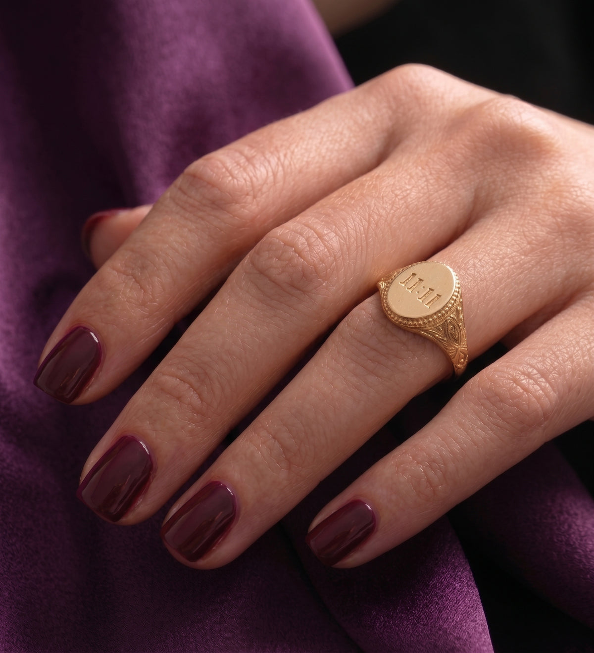 11:11 signet ring worn, hand resting on purple fabric
