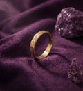 Birth flower band ring standing on purple velvet beside an amethyst stone