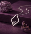Birth flower ring holder necklace in a silver tone on a plum box