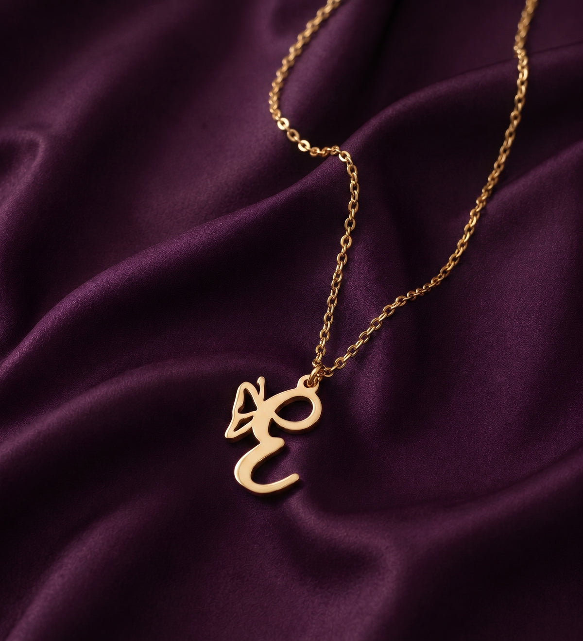 Gold butterfly initial necklace laid on purple satin, script letter pendant with a butterfly