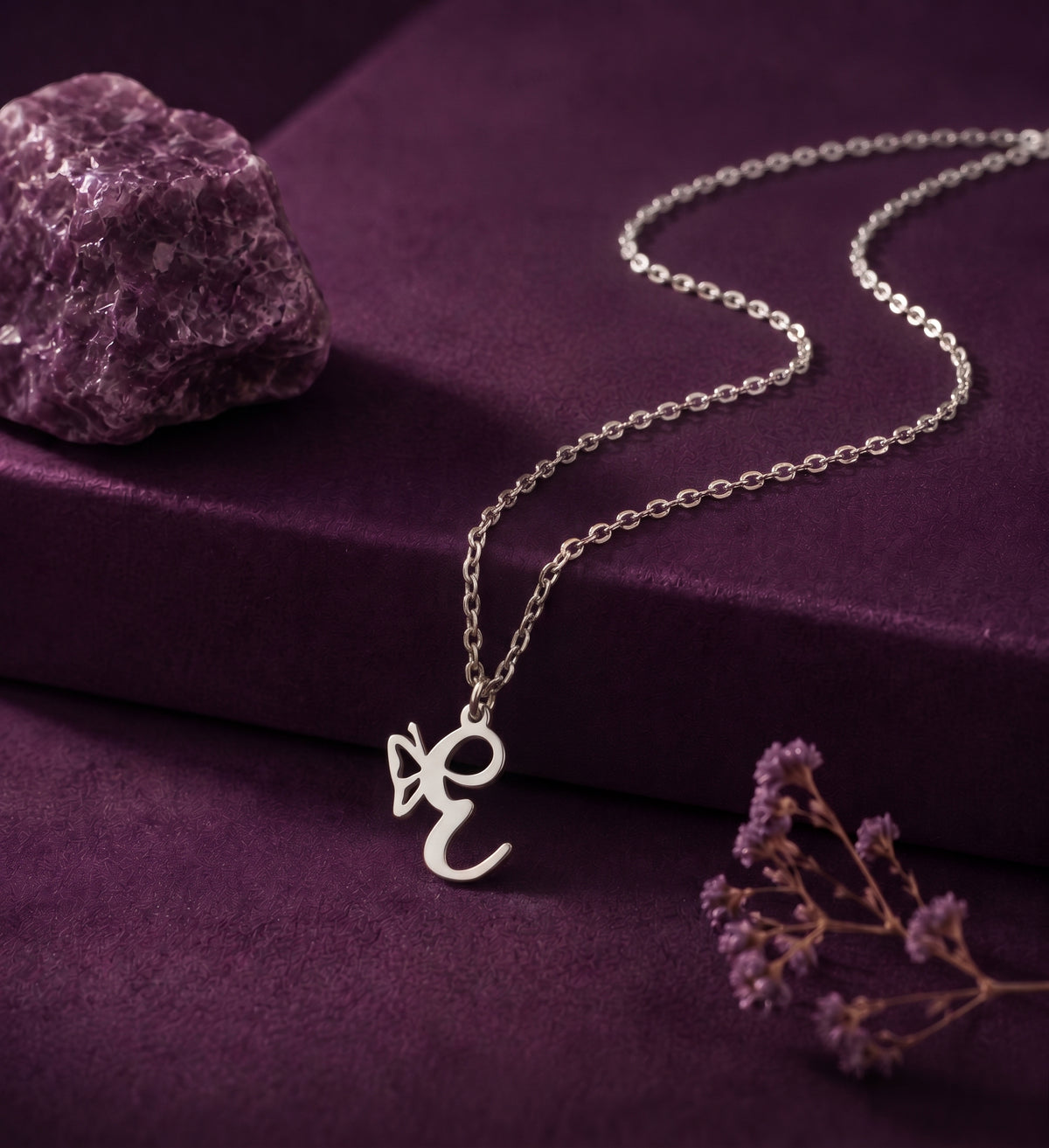 Silver butterfly initial necklace on purple velvet beside an amethyst stone