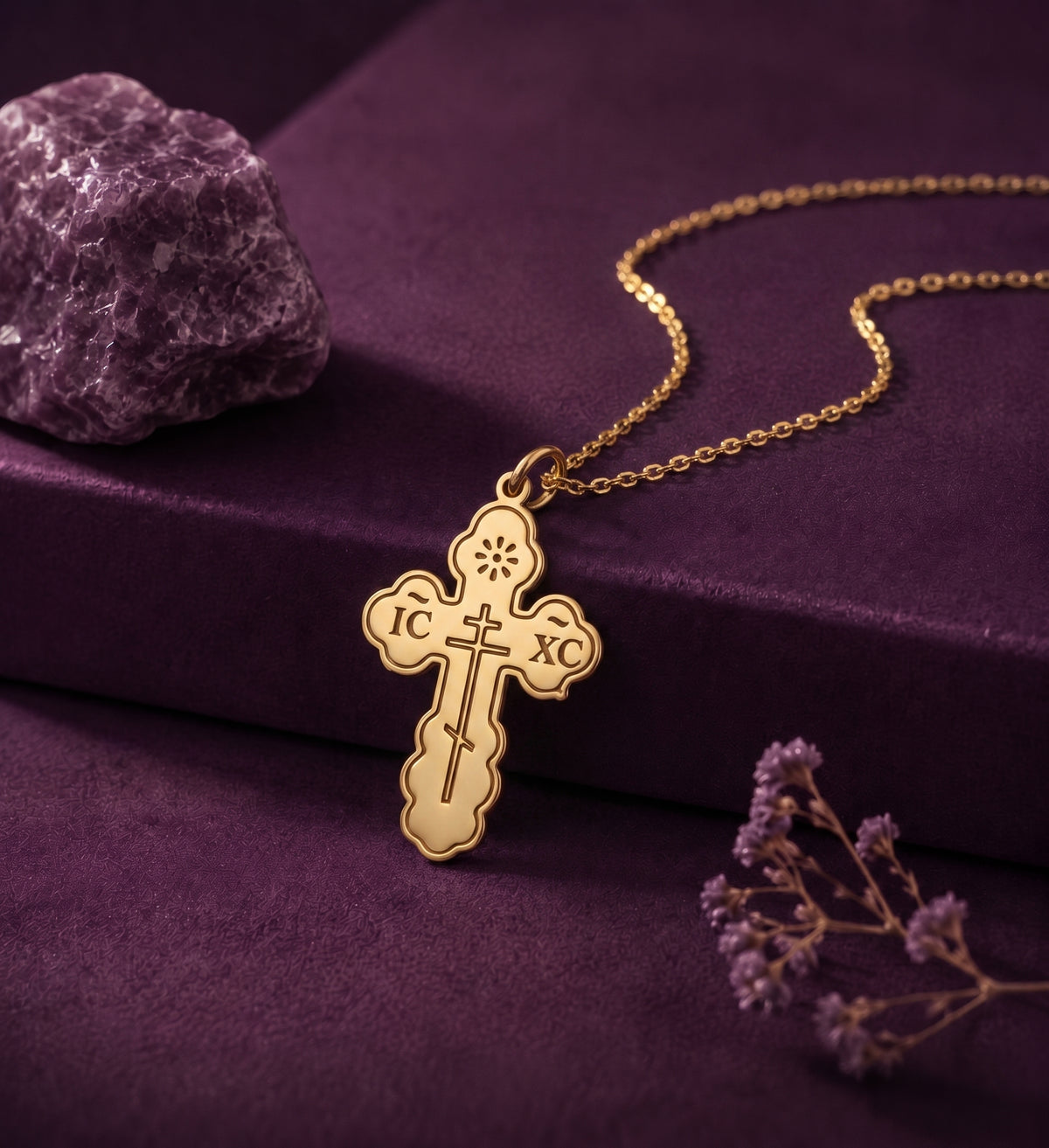 Engraved cross necklace on a plum box beside an amethyst stone