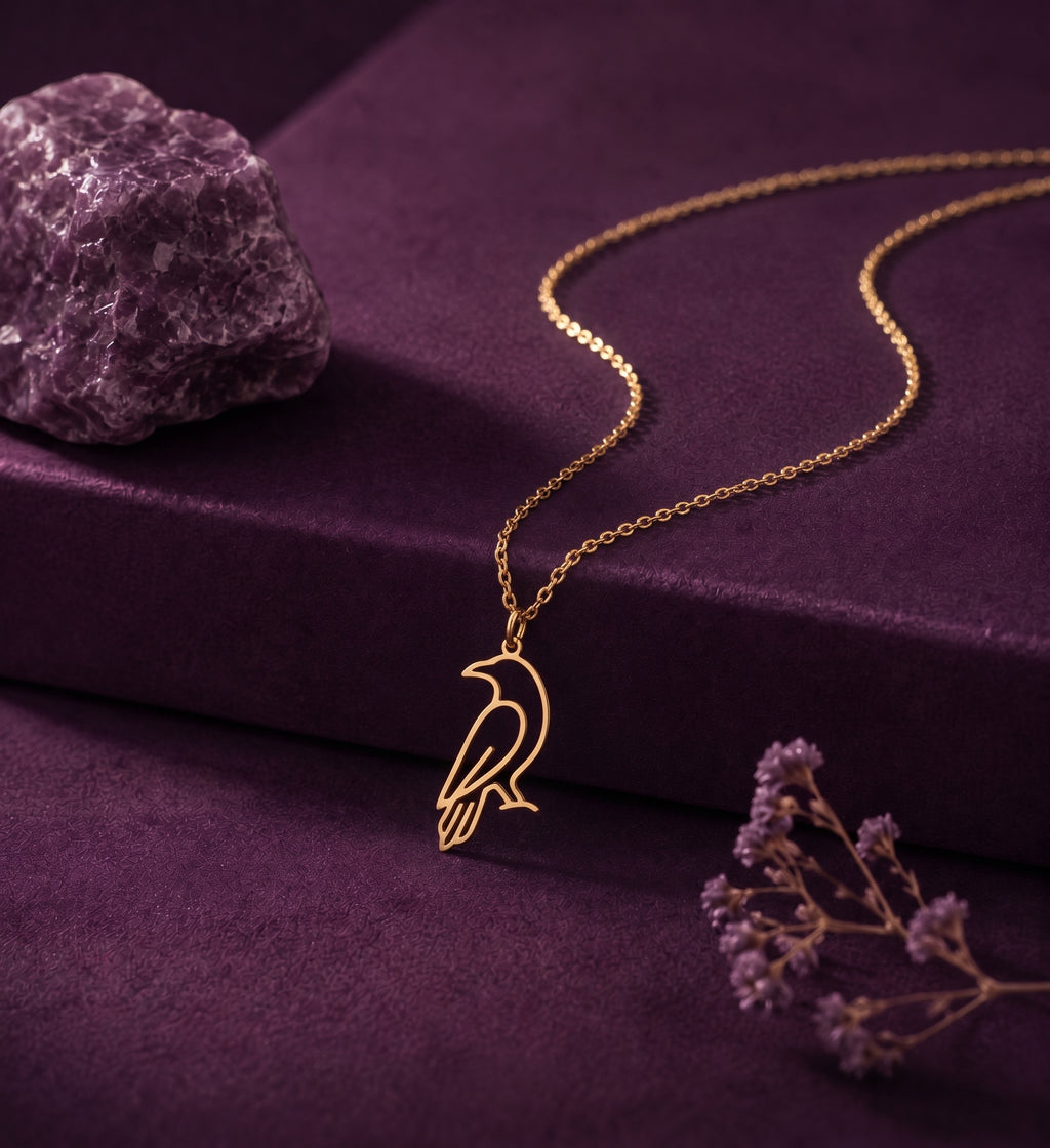 Crow outline necklace on a plum box beside an amethyst stone