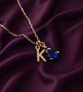 Necklace with a K initial charm and a blue pear-shaped stone on purple satin