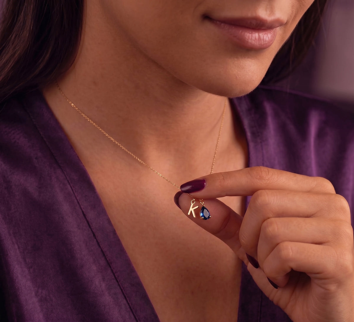 Initial and birthstone charms held between two fingers
