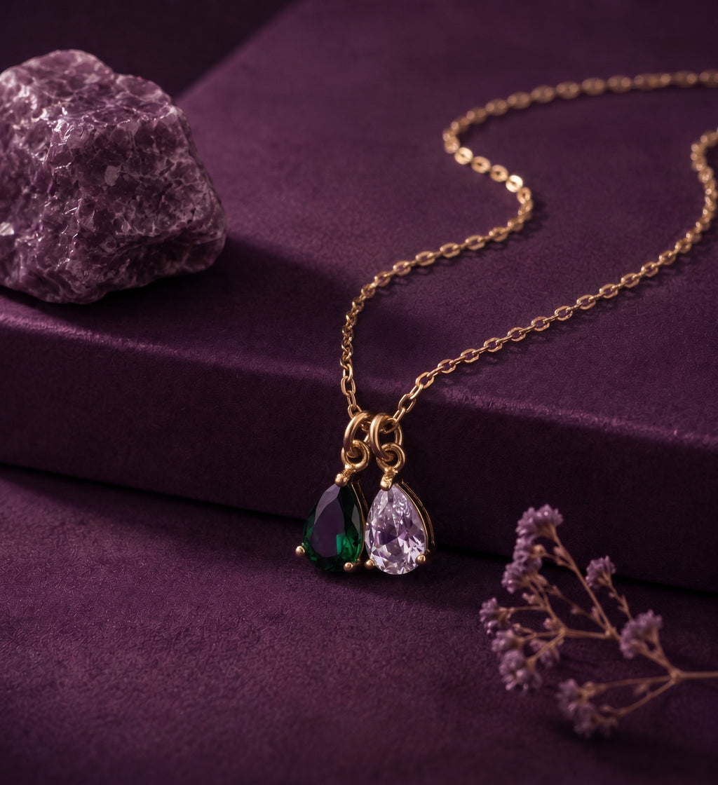 Necklace with a green and a clear pear-shaped stone on a plum box