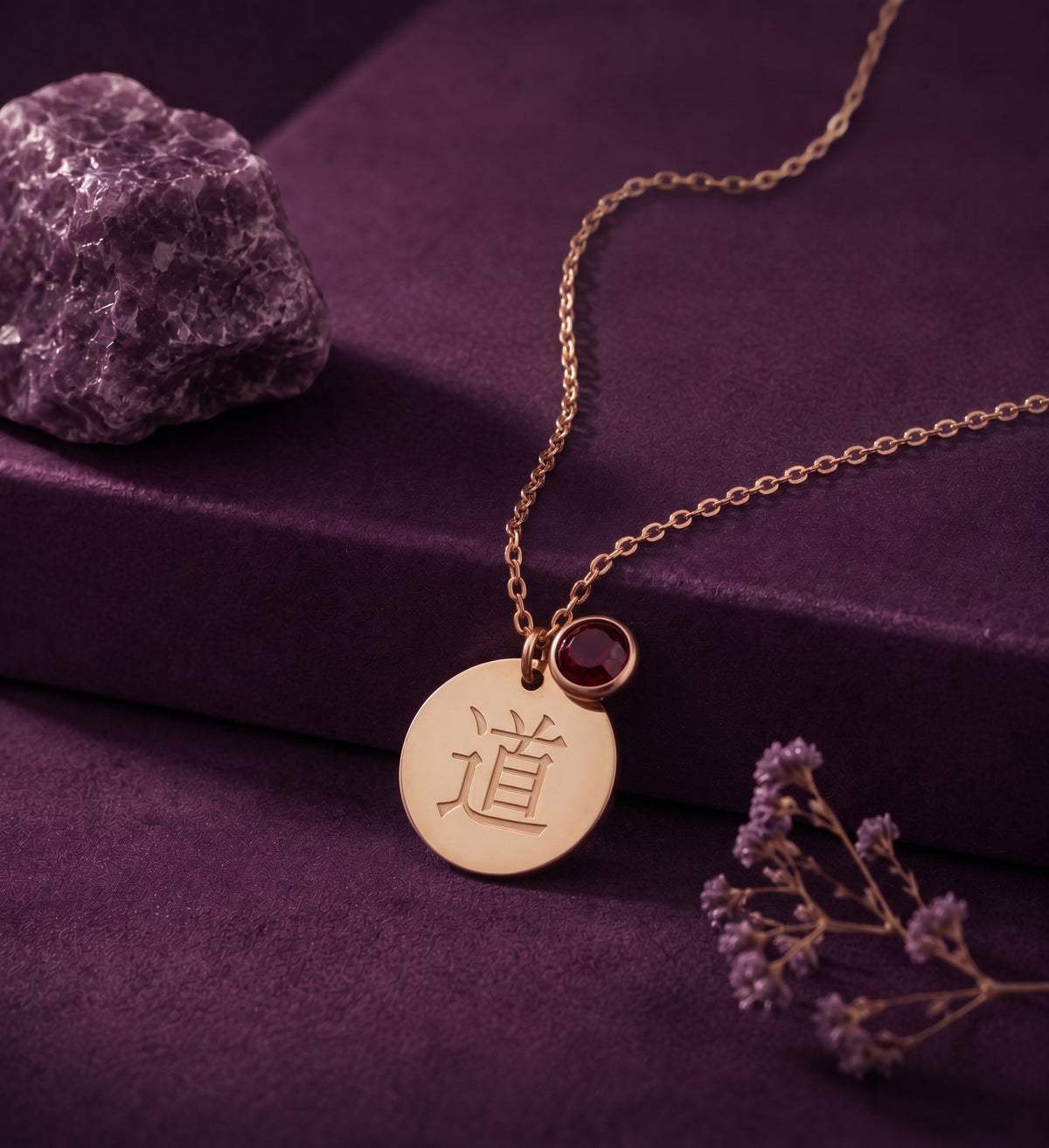 Kanji disc necklace with a red stone on a plum box beside an amethyst stone