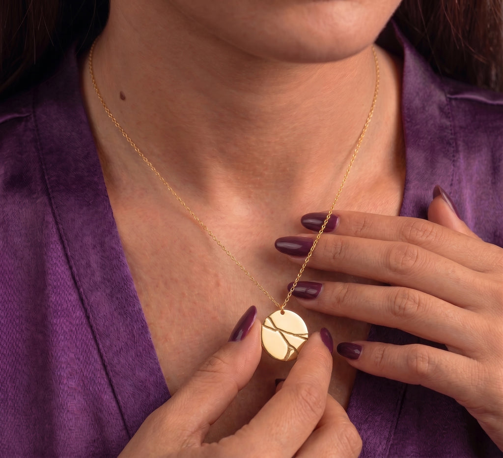 Kintsugi disc necklace worn, pendant held between the fingers