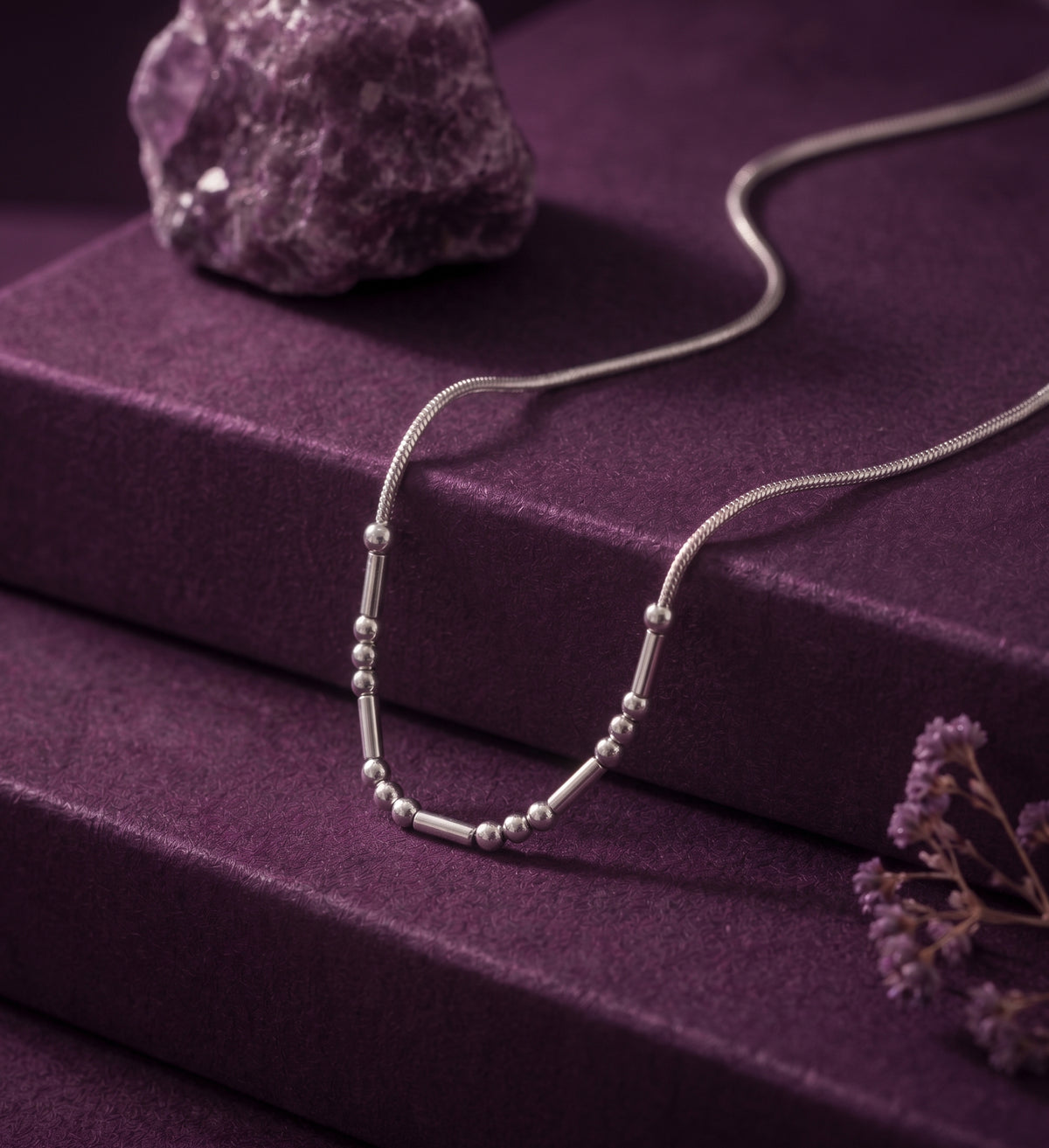 Morse code necklace laid on purple velvet beside an amethyst stone